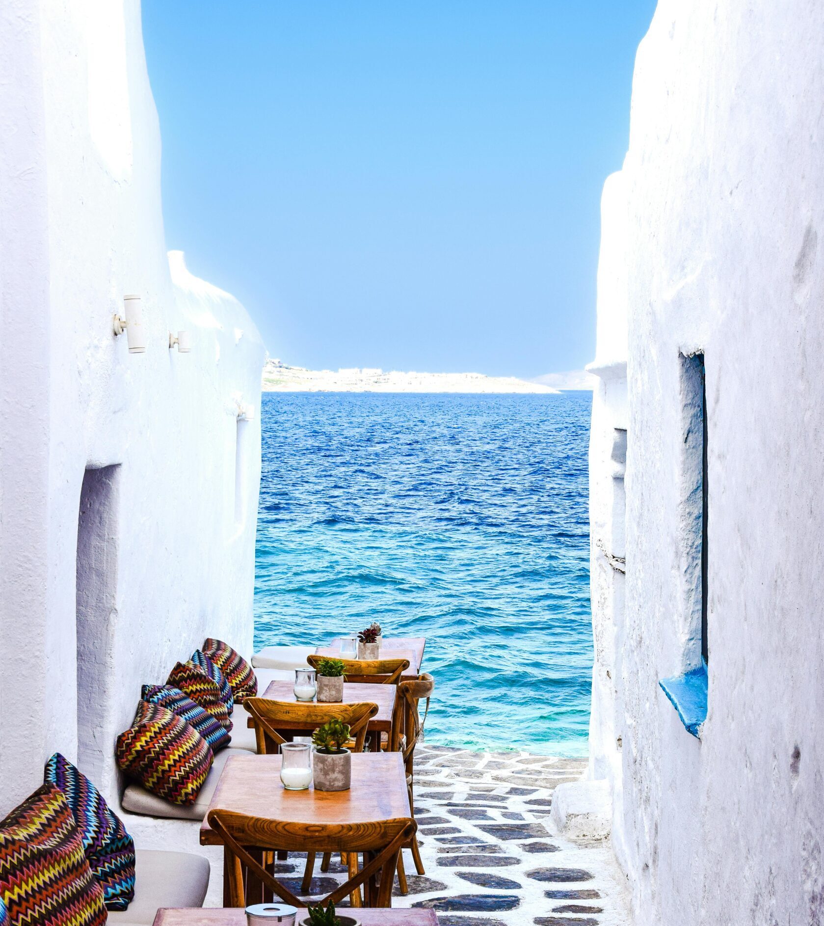 Picturesque Greek alley with tables by the sea, showcasing a serene and inviting setting.