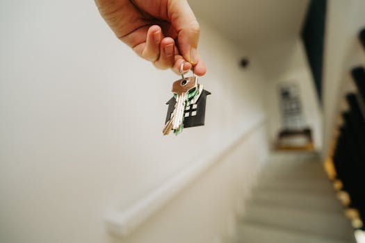 Close-up of a hand holding a keychain in the shape of a house, symbolizing real estate and property ownership.