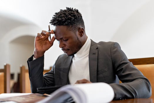 A focused businessman in a suit examines documents while deep in thought in an office setting.