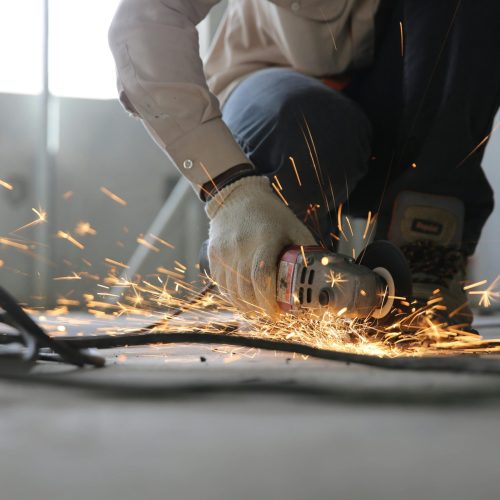 A skilled industrial worker uses a grinder creating a burst of sparks indoors.